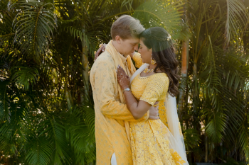 Ummae and Ryan embracing in yellow haldi outfits in front of tropical greenery