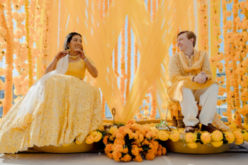 Ummae and Ryan seated during their haldi ceremony surrounded by yellow floral decor
