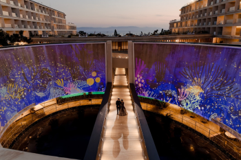 Ummae and Ryan walking along a dramatic illuminated walkway at Dreams Bahia Mita with colorful underwater mural projections on the surrounding walls.
