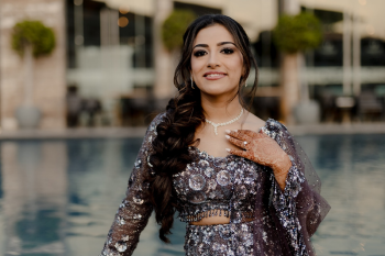 Ummae posing by the water in her silver sangeet lehenga with intricate beadwork and mehndi during an Indian destination wedding celebration.

Caption: Ummae shines in her intricately beaded silver sangeet lehenga, posing by the water before the evening’s celebration begins.