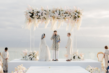 Indian oceanfront wedding ceremony with white floral mandap and bride and groom exchanging vows by the sea