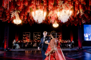 Ummae and Ryan sharing their first dance beneath a red floral ceiling during their Indian wedding reception
