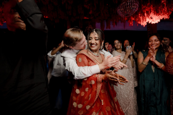 Ryan and Ummae embracing and clapping on the dance floor during their Indian wedding reception celebration.

