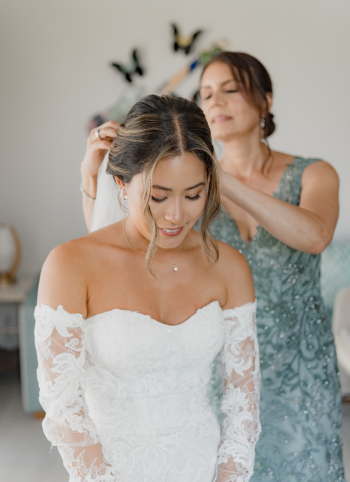 Bride in lace wedding dress getting ready with hair and veil being adjusted before a destination wedding ceremony.
