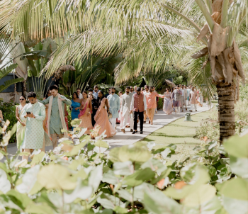 Wedding guests walking together through a palm-lined pathway during a baraat procession at an Indian destination wedding.