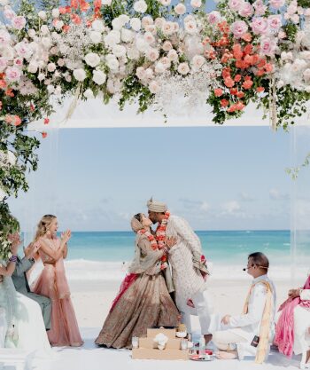 Bride and groom at a Hindu wedding ceremony under a floral mandap on the beach with ocean views during a destination wedding.