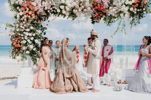 Bride and groom exchange garlands during a beachfront Hindu wedding ceremony at Hard Rock Punta Cana under a floral mandap with ocean views in the Dominican Republic.