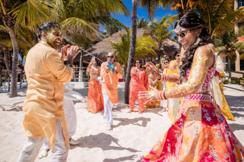 Bride and groom laughing on the beach while guests spray water guns after haldi ceremony at Indian destination wedding