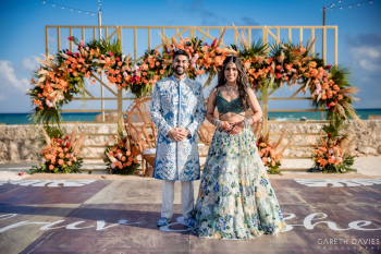 Indian bride and groom posing on decorated dance floor with floral backdrop during sangeet at destination wedding.