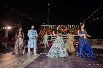 Bride and groom performing choreographed dance with family and friends during Indian sangeet celebration at night.