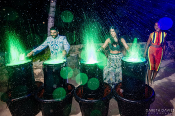 Bride and groom playing illuminated water drums with performers during sangeet entertainment at destination wedding.