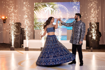 Bride and groom first dance with indoor sparklers on dance floor during Indian wedding reception in ballroom.
