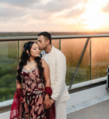 Indian bride and groom posing at sunset on a resort rooftop terrace at Generations Riviera Maya, bride wearing a beaded burgundy floral lehenga with intricate mehndi, groom in a white linen blazer