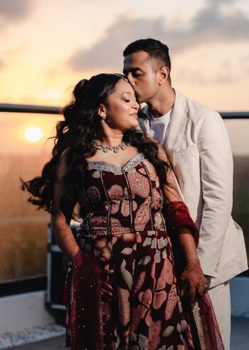 Indian bride in a burgundy floral lehenga with mehndi-covered hands and groom in a cream suit sharing a quiet moment on Sky Terrace at Generations Riviera Maya.