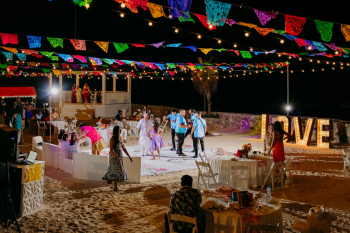 Beachfront Indian sangeet celebration at the White Gazebo venue with colorful papel picado banners, string lights, dancing guests, and oceanfront views at night. Beachfront Indian sangeet celebration at the White Gazebo venue with colorful papel picado banners, string lights, dancing guests, and oceanfront views at night.