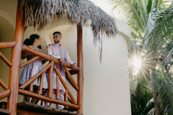 Malena and Eshwar standing together on a tropical balcony before their wedding celebrations in Mexico