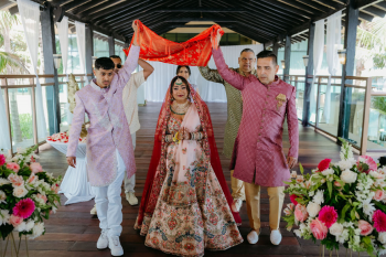 Malena making her bridal entrance beneath a red dupatta during her Hindu wedding ceremony at the Pier Deck at Generations Riviera Maya