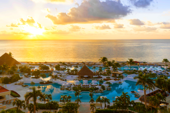 Sunset view over expansive resort pools with palm trees, lounge areas, and ocean horizon creating a relaxed beachfront setting