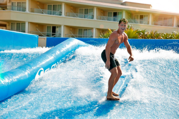 Guest riding the FlowRider surf simulator with water waves in a resort activity area, showcasing an on-site surfing experience