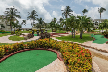 Outdoor mini golf course surrounded by palm trees, landscaped greenery, and walking paths at a beachfront resort