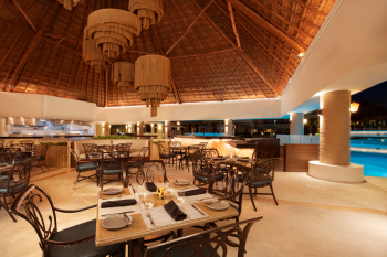 Open-air restaurant with thatched roof, warm lighting, and poolside seating creating a relaxed dining atmosphere