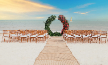 Beach wedding setup with aisle, wooden chairs, and a floral arch facing the ocean for a destination ceremony