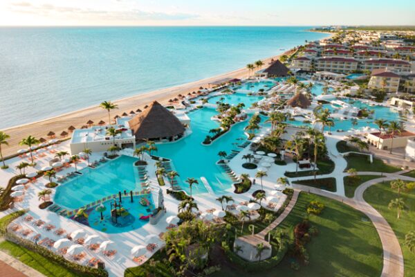 Aerial view of a large beachfront resort with interconnected turquoise pools, palm-lined pathways, swim-up bars, and a sandy shoreline stretching along the Caribbean coast
