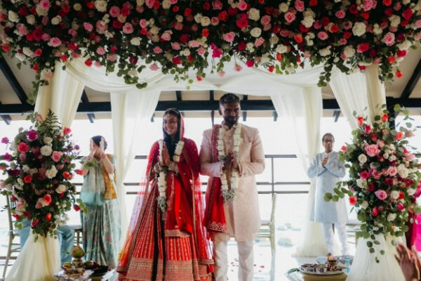 Katherine and Marun stand beneath a floral mandap during their Hindu wedding ceremony at the Pier Deck at Generations Riviera Maya.