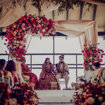 Meha and Gilbert participate in traditional
wedding rituals beneath a cream-draped mandap adorned with vibrant pink, red,
and orange florals. Meha and Gilbert participate in traditional
wedding rituals beneath a cream-draped mandap adorned with vibrant pink, red,
and orange florals.