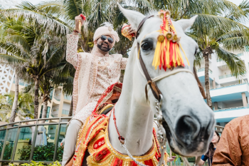 Groom in a cream sherwani riding a white horse decorated with red and gold ceremonial regalia during the baraat procession at Ripal and Palak's Indian wedding at Generations Riviera Maya. Groom in a cream sherwani riding a white horse decorated with red and gold ceremonial regalia during the baraat procession at Ripal and Palak's Indian wedding at Generations Riviera Maya.