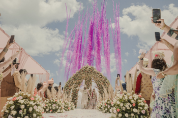 Niyati and Rachit celebrate their Indian destination wedding ceremony at Moon Palace The Grand - Cancun as vibrant magenta smoke bombs erupt behind a floral mandap, creating a dramatic moment while guests cheer. Niyati and Rachit celebrate their Indian destination wedding ceremony at Moon Palace The Grand - Cancun as vibrant magenta smoke bombs erupt behind a floral mandap, creating a dramatic moment while guests cheer.