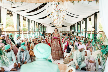 Komal makes her bridal entrance during a Sikh destination wedding in the Riviera Maya, walking beneath flowing white drapery and suspended floral installations while family and guests gather for the ceremony. Komal makes her bridal entrance during a Sikh destination wedding in the Riviera Maya, walking beneath flowing white drapery and suspended floral installations while family and guests gather for the ceremony.
