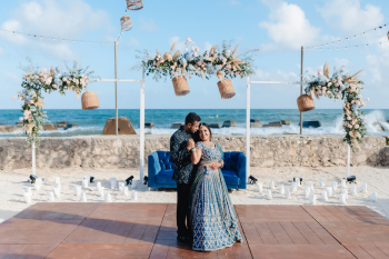 Indian bride and groom posing at beachfront sangeet venue with floral arch and ocean backdrop at El Dorado Royale, Riviera Maya
