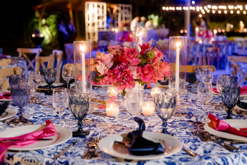 Indian destination wedding welcome dinner tablescape with hot pink floral centerpiece, candlelight, and blue patterned linens at Dreams Bahia Mita, Mexico