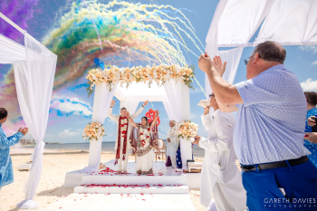 Gopi and Nick celebrate their beachfront Indian wedding ceremony at Royalton Splash Riviera Cancun as colorful smoke effects fill the sky. Gopi and Nick celebrate their beachfront Indian wedding ceremony at Royalton Splash Riviera Cancun as colorful smoke effects fill the sky.