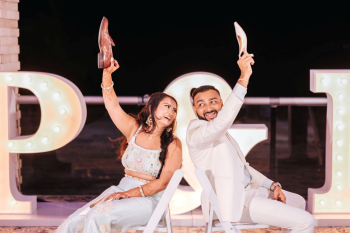 Bride and groom playing the shoe game at an Indian wedding Welcome Night in front of a lit-up marquee sign Bride and groom playing the shoe game at an Indian wedding Welcome Night in front of a lit-up marquee sign