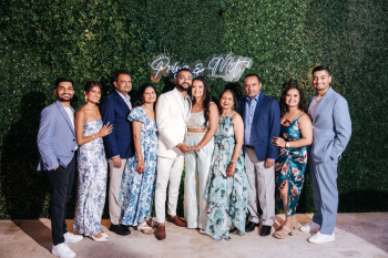 Indian wedding Welcome Night family portrait in front of a greenery wall with a neon couple's sign Indian wedding Welcome Night family portrait in front of a greenery wall with a neon couple's sign