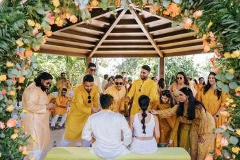 Wide view of guests in yellow at an Indian wedding Haldi ceremony under a wooden gazebo Wide view of guests in yellow at an Indian wedding Haldi ceremony under a wooden gazebo
