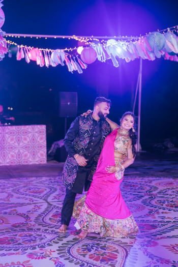 Couple performing a dance during an Indian wedding Sangeet under a string of tassels and an ornate dance floor with a floral design. Couple performing a dance during an Indian wedding Sangeet under a string of tassels and an ornate dance floor with a floral design.