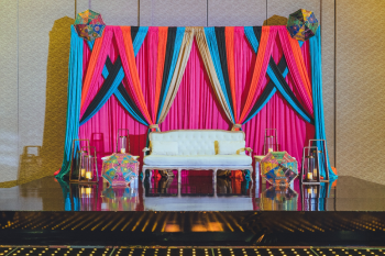 Colorful draped stage backdrop with embroidered umbrellas at an Indian wedding Sangeet Colorful draped stage backdrop with embroidered umbrellas at an Indian wedding Sangeet