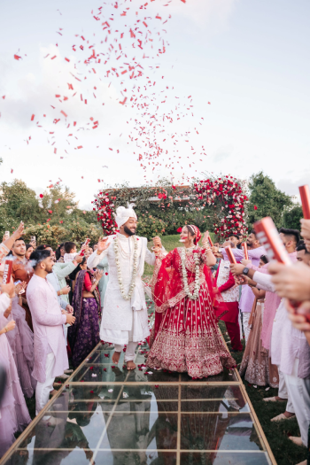 Indian bride and groom walking down the aisle in front of their wooden pergola mandap with rose-covered posts for an outdoor Indian wedding ceremony Indian bride and groom walking down the aisle in front of their wooden pergola mandap with rose-covered posts for an outdoor Indian wedding ceremony