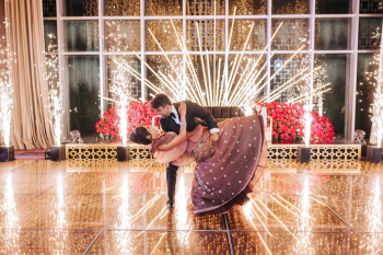 Bride and groom perform their first dance in front of a radiating gold sunburst light fixture and cold sparklers on an LED dance floor at an Indian wedding reception Bride and groom perform their first dance in front of a radiating gold sunburst light fixture and cold sparklers on an LED dance floor at an Indian wedding reception