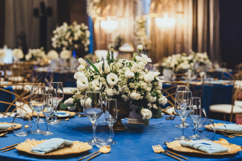Blue linens, gold charger plates and white floral centerpieces at an Indian wedding reception in a ballroom. Blue linens, gold charger plates and white floral centerpieces at an Indian wedding reception in a ballroom.