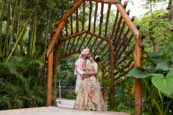 Khyati and Parth posing beneath a wooden garden pavilion at Generations Riviera Maya during their Indian destination wedding in Riviera Maya, Mexico. Khyati and Parth posing beneath a wooden garden pavilion at Generations Riviera Maya during their Indian destination wedding in Riviera Maya, Mexico.