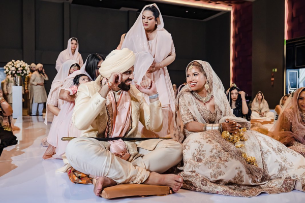Sikh groom in a cream turban and bride in a blush gold lehenga smiling during their Anand Karaj ceremony at Planet Hollywood Cancun, Mexico