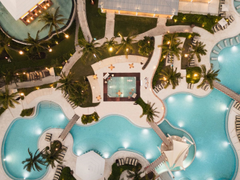 Aerial nighttime view of the free-form swimming pools at Dreams Jade Resort and Spa, lit up and surrounded by palm trees and lounge chairs. Aerial nighttime view of the free-form swimming pools at Dreams Jade Resort and Spa, lit up and surrounded by palm trees and lounge chairs.