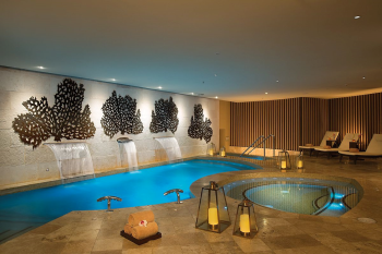 Indoor hydrotherapy pool at the Dreams Jade Resort and Spa spa, with coral-inspired wall art, waterfalls, and a whirlpool tub. Indoor hydrotherapy pool at the Dreams Jade Resort and Spa spa, with coral-inspired wall art, waterfalls, and a whirlpool tub.