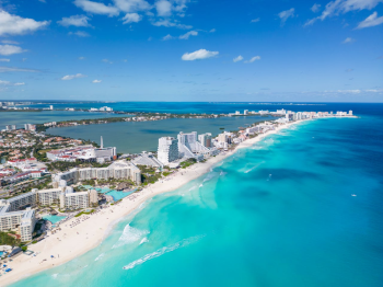 Aerial view of the Cancun Hotel Zone in Mexico, with beachfront resorts along white sand and turquoise Caribbean water on one side and Nichupté Lagoon on the other, a popular destination for South Asian weddings. Aerial view of the Cancun Hotel Zone in Mexico, with beachfront resorts along white sand and turquoise Caribbean water on one side and Nichupté Lagoon on the other, a popular destination for South Asian weddings.