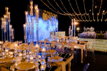 Ummae and Ryan's outdoor sangeet at night, with mirrored tables, tall candelabra centerpieces, clear ghost chairs, a light-up dance floor and an LED screen under string lights, showing how a resort lawn becomes its own event space for an Indian destination wedding. Ummae and Ryan's outdoor sangeet at night, with mirrored tables, tall candelabra centerpieces, clear ghost chairs, a light-up dance floor and an LED screen under string lights, showing how a resort lawn becomes its own event space for an Indian destination wedding.